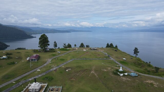 Aerial view of Tara Bunga overlooking the vast expanse of Lake Toba with grassy hills, winding paths, and scattered trees in Tampahan, North Sumatra, Indonesia.