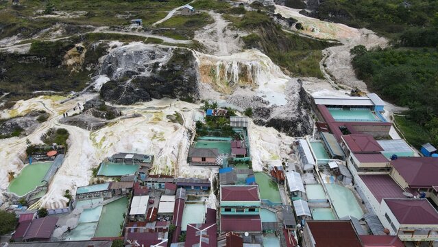 Aerial view of the geothermal hot springs in Sipoholon with white mineral deposits, turquoise pools, and surrounding buildings in Tarutung, North Sumatra, Indonesia.