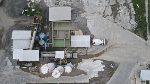 Aerial view of the concrete batching plant at the Dhoho International Airport construction site with industrial silos and a cement mixer truck in Kecamatan Grogol, Jawa Timur, Indonesia.