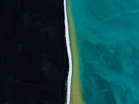 Aerial view of a black sand beach meeting turquoise glacial water in Iceland.
