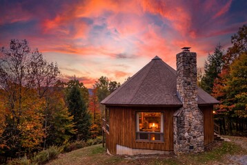 Fototapeta premium Cozy wooden cabin sunset with autumn foliage and warm glowing fireplace