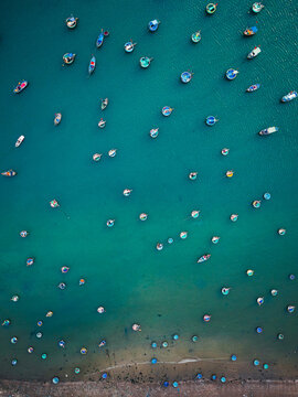 Aerial view of numerous traditional round basket boats scattered across the vibrant turquoise water near the sandy coastline of Vietnam.