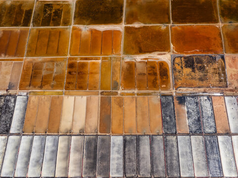 Aerial view of salt pans in Vietnam, showing rectangular plots with varying shades of brown, white, and grey indicating different stages of salt production.