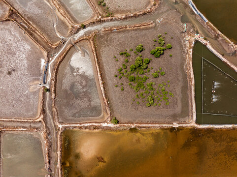 Aerial view of salt pans and aquaculture ponds with geometric shapes and a patch of green vegetation in Vietnam.