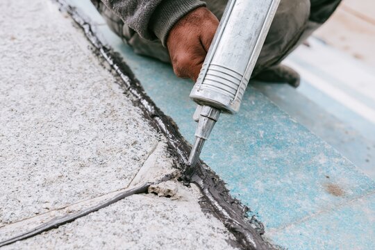 Close up of a worker applying dark asphalt sealant with a caulk gun to stone steps for a home maintenance and outdoor repair scene