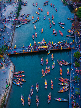 Aerial view of traditional wooden boats floating on the river with glowing lanterns and people walking on the bridge in Vietnam.