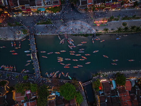 Aerial view of the Thu Bon River in Hoi An with numerous small wooden boats, illuminated lanterns, and historic architecture along the riverbanks in Vietnam.