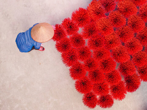 Aerial view of a person in a conical hat arranging vibrant red incense bundles on a concrete surface in Vietnam.