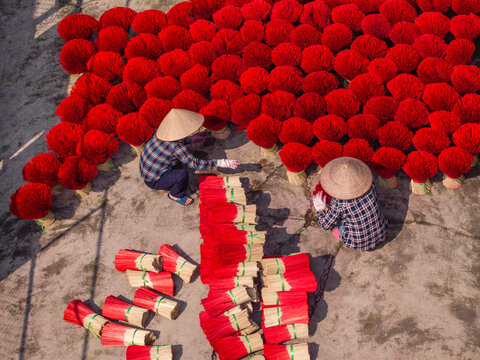 Aerial view of workers wearing traditional conical hats while drying bright red incense sticks on the ground in Vietnam.