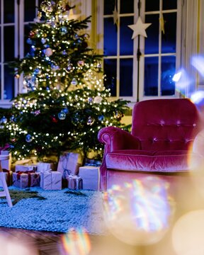 Decorated Christmas tree and magenta velvet armchair in a glowing festive room with wrapped gifts for holiday home and seasonal greeting campaigns