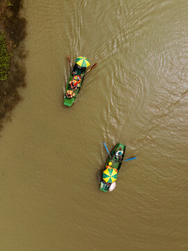 Aerial view of two small boats with people and colorful umbrellas rowing on a river in Vietnam.