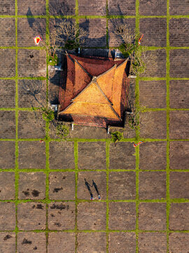 Aerial view of a traditional pavilion with an orange tiled roof set in a stone grid courtyard with grass, with two people holding hands casting long shadows in Vietnam.