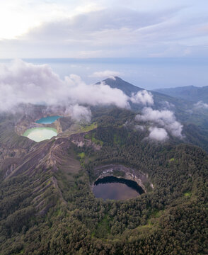 Aerial view of the three colored crater lakes of Kelimutu National Park surrounded by lush volcanic forest and mountain peaks in Detusoko, East Nusa Tenggara, Indonesia.