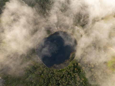 Aerial view of the volcanic crater lake in Kelimutu National Park surrounded by lush forest and drifting clouds in Detusoko, East Nusa Tenggara, Indonesia.