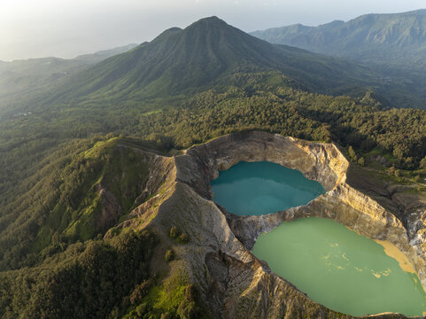 Aerial view of the turquoise and green crater lakes of Kelimutu National Park surrounded by lush volcanic mountains and dense forest in Detusoko, East Nusa Tenggara, Indonesia.