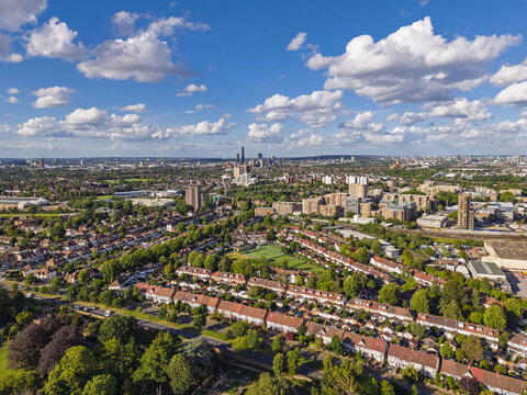 Aerial view of the residential neighborhood with rows of houses, lush green trees, and a distant city skyline under a bright blue sky in Brentford, England, United Kingdom.