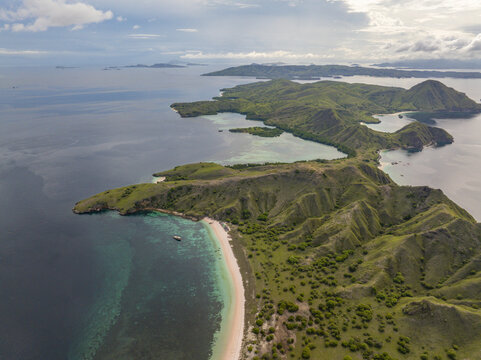 Aerial view of Pink Beach with its unique pink sand, turquoise waters, and surrounding lush green hills in East Nusa Tenggara, Indonesia.