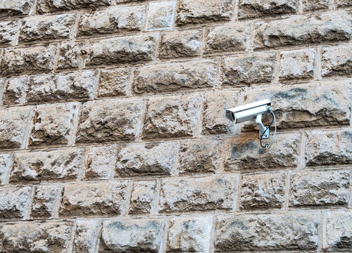 Security camera mounted on rough stone wall outdoors, surveillance system on aged masonry building exterior, concept of urban security and public monitoring