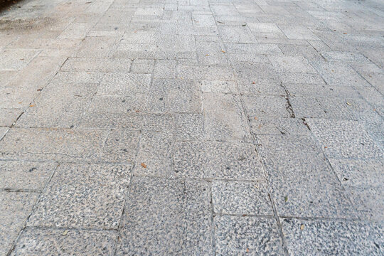 Granite stone pavement tiles forming symmetrical pattern on outdoor plaza, gray textured surface with visible grout joints, urban hardscape background concept