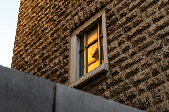 Stone building exterior with rustic textured limestone wall and single window reflecting warm golden sunset light, architectural detail and urban design concept