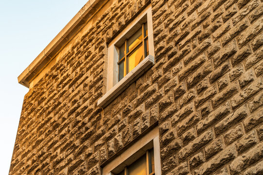 Stone building exterior with rustic rough-cut limestone blocks and framed windows lit by warm golden hour light, architectural detail of classic masonry facade