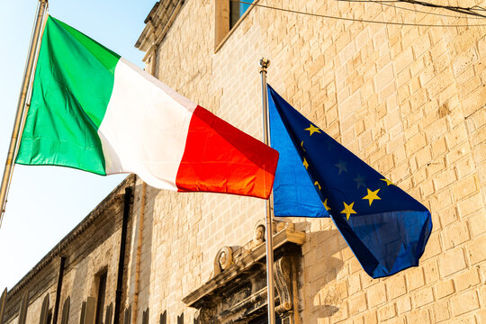 Italian and European Union flags waving together on stone building facade, symbolizing Italy EU membership, political unity and European identity concept