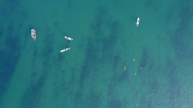 Aerial view of Circuito de Playas with a small boat, paddleboarders, and a swimmer in the turquoise water of Chorrillos, Provincia de Lima, Peru.
