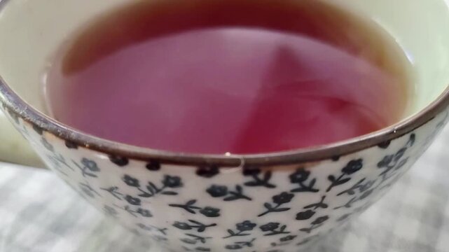 High angle close-up video showing a steaming cup of tea placed on a dining table. The camera is fixed, capturing the rising vapor in the warm morning light, creating a calm and intimate atmosphere.