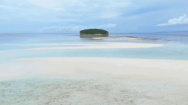 Aerial view of Pasir Timbul Mansuar sandbar surrounded by turquoise waters and a small lush island under a cloudy sky in Raja Ampat, Papua Barat Daya, Indonesia.