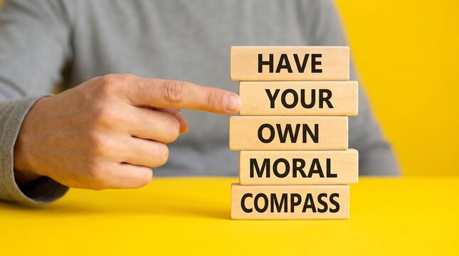 Moral compass concept on wooden blocks, person pointing at ethical message, integrity and values metaphor on yellow background