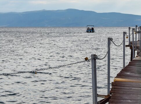 View of a wooden pier extending into the calm waters of Lake Ohrid with a small boat in the distance and mountains in Ohrid, Municipality of Ohrid, North Macedonia.