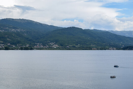 View of Lake Ohrid with small boats on the water and mountains in the background under a cloudy sky in Ohrid, Municipality of Ohrid, North Macedonia.