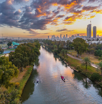 Aerial view of Yarkon River at sunset with rowers in boats, lush parkland, and the city skyline in the background in Tel Aviv-Yafo, Tel Aviv District, Israel.
