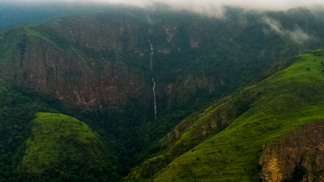 Aerial view of the waterfall cascading down the lush green cliffs of the mountain range in Likpe Bakwa, Volta Region, Ghana.