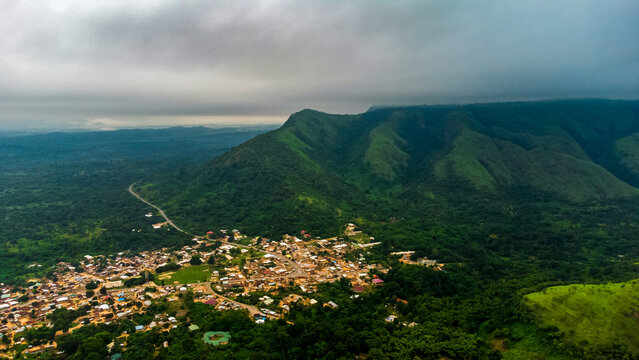Aerial view of the town of Likpe Bakwa nestled among lush green mountains and dense tropical forests under a cloudy sky in Likpe Bakwa, Volta Region, Ghana.