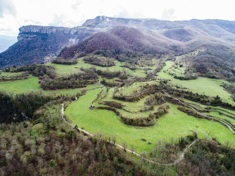 Aerial view of green terraced fields and rolling hills with dirt paths and rocky cliffs in the background in Rupit, Catalonia, Spain.