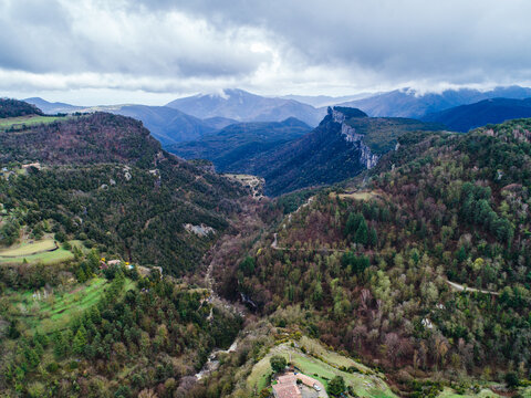 Aerial view of the rugged landscape surrounding the village of Rupit, featuring dense forests, deep valleys, and distant mountains under a cloudy sky in Rupit, Catalonia, Spain.