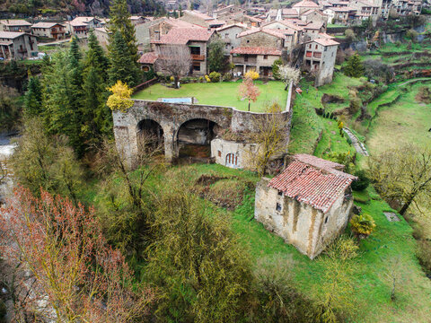 Aerial view of historic stone houses and lush green gardens in the medieval village of Rupit, featuring traditional architecture and rural landscape in Rupit, Catalonia, Spain.