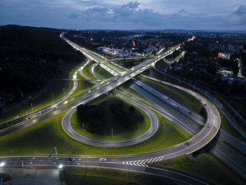 Aerial view of an illuminated highway interchange at night with car light trails and surrounding green landscape, Wieliczka, Lesser Poland Voivode, Poland.