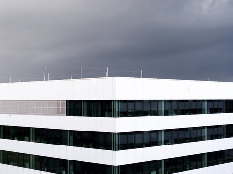 Aerial view of a modern white office building with dark glass windows under a cloudy sky in Poland.