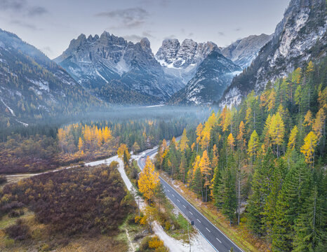 Aerial view of Durrensee surrounded by autumn-colored larch trees, a winding road, and the dramatic peaks of the Dolomites in Toblach, Trentino-Alto AdigeS, Italy.