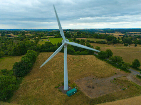 Aerial view of a wind turbine standing in a rural landscape with green fields and trees in Mansfield, England, United Kingdom.