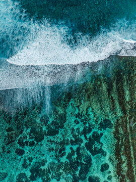 Aerial view of turquoise ocean waves breaking over a vibrant coral reef in the clear tropical waters of Mauritius.