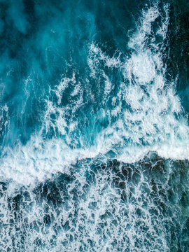Aerial view of turquoise ocean waves crashing against a coral reef with white sea foam and deep blue water, Mauritius.