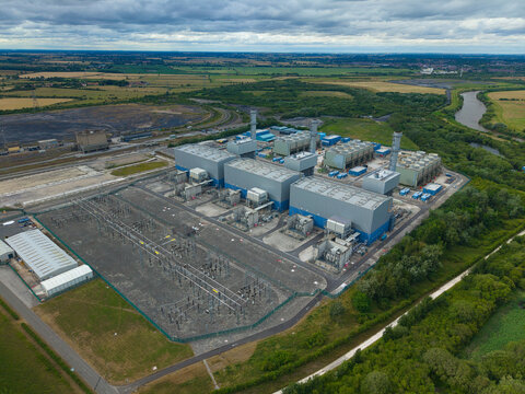 Aerial view of West Burton Power Station featuring industrial buildings, an electrical substation, and surrounding green fields near the river in West Burton, England, United Kingdom.