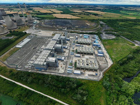 Aerial view of West Burton Power Station featuring its iconic cooling towers, industrial infrastructure, and surrounding green fields in West Burton, England, United Kingdom.