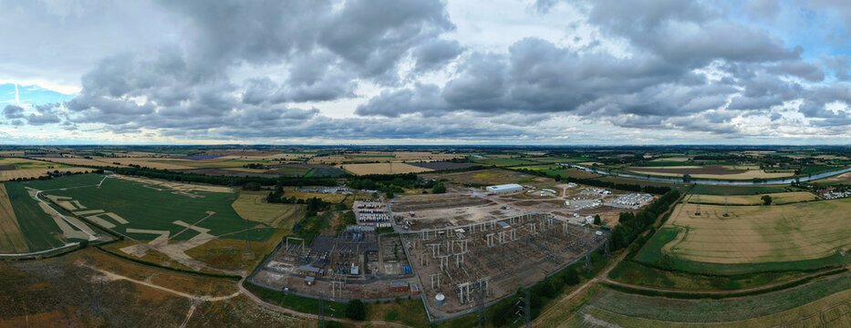 Aerial view of the National Grid High Marnham Substation with electrical infrastructure, transformers, and power lines, surrounded by rural fields and a river in Newark, England, United Kingdom.