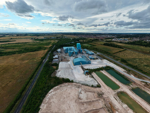 Aerial view of Saint Gobain Formula industrial plant with large blue buildings, gypsum processing areas, and surrounding fields in New Balderton, England, United Kingdom.
