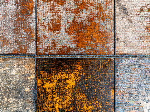 Aerial view of a weathered, grid-patterned surface with rusted metal tiles and textured stone blocks in Mauritius.