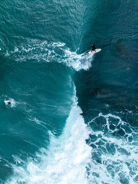 Aerial view of a surfer riding a turquoise wave with white foam patterns in the ocean off the coast of Mauritius.